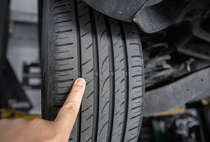 Mechanic pointing with hand at tyre wear indicator at car service center.